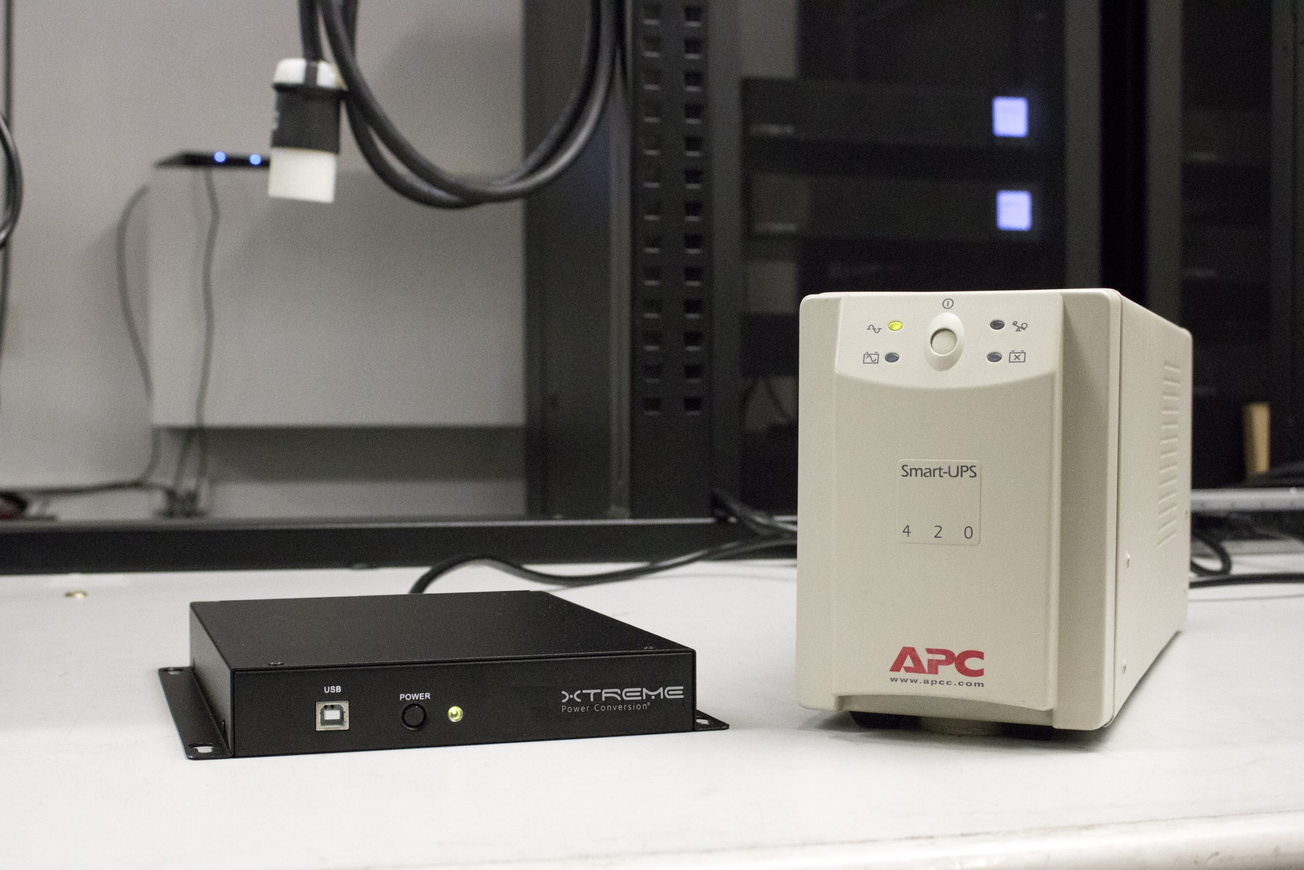 Xtreme Power J60 ultra-compact lithium UPS beside a conventional tower UPS of similar capacity, showing the J60's far slimmer profile