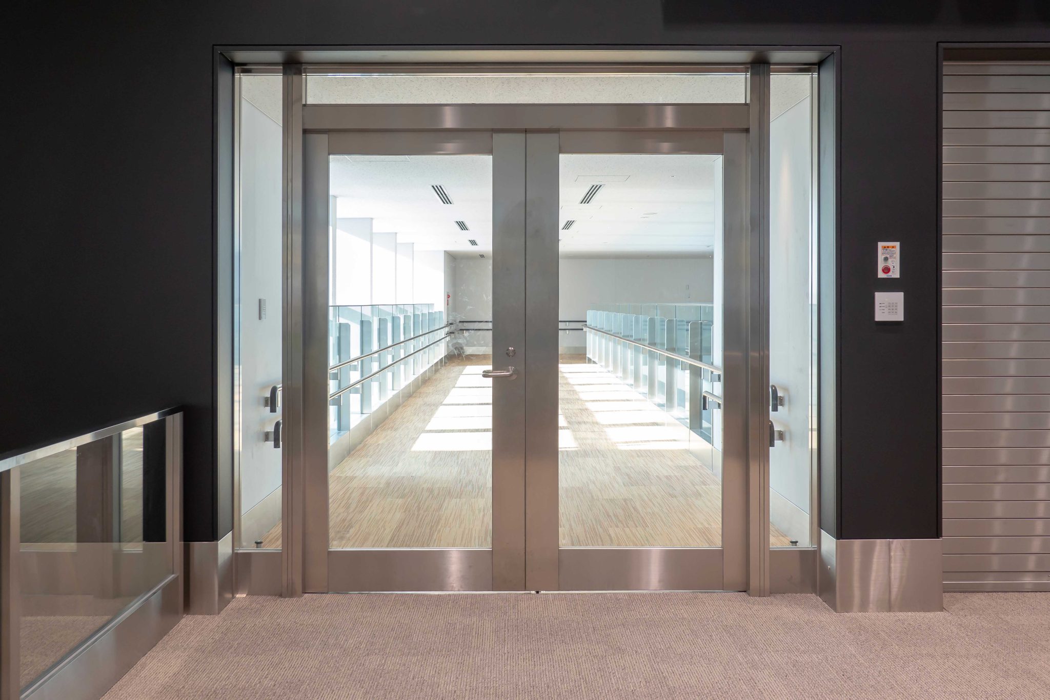 Commercial glass and stainless steel automatic doors in a high-end building — access control panel visible on right wall, J60 UPS protects the door operator controller