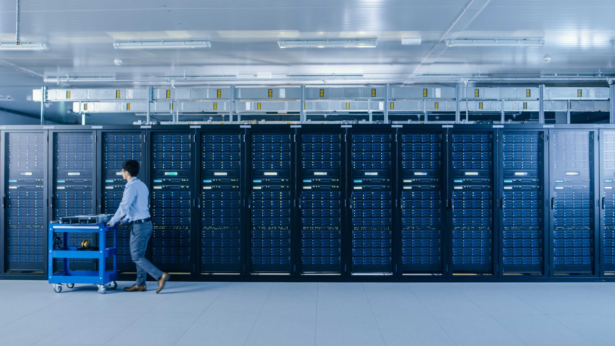Technician moving equipment past a row of server racks in a data center where uptime and scalability are critical